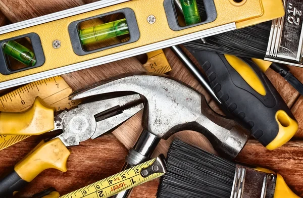 Level, claw hammer, pliers, screwdriver, paintbrushes and tape measures on a wood surface